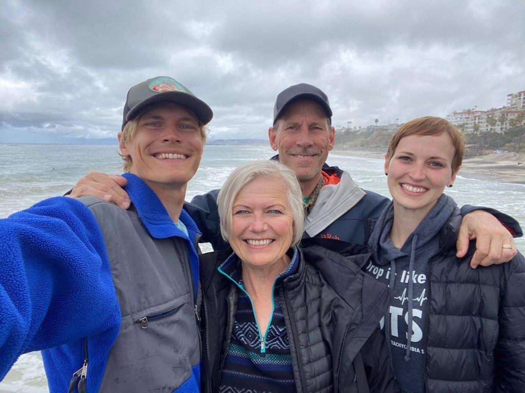 Greg Muhonen and his wife and two children smile for a family photo with a beach as a backdrop.